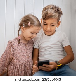 Siblings brother boy hold smartphone with girl sister children use mobile phone smartphone at home in room watch video make a call or play online games leisure family concept real people copy space - Shutterstock ID 2395054043