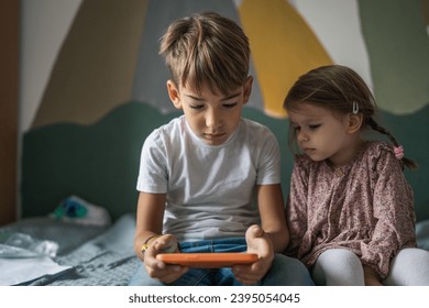 Siblings brother boy hold smartphone with girl sister children use mobile phone smartphone at home in room watch video make a call or play online games leisure family concept real people copy space - Shutterstock ID 2395054045