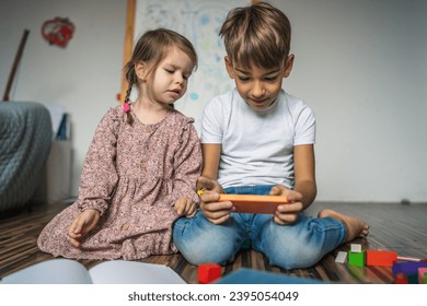 Siblings brother boy hold smartphone with girl sister children use mobile phone smartphone at home in room watch video make a call or play online games leisure family concept real people copy space - Shutterstock ID 2395054049