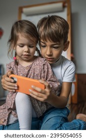 Siblings brother boy hold smartphone with girl sister children use mobile phone smartphone at home in room watch video make a call or play online games leisure family concept real people copy space - Shutterstock ID 2395054055