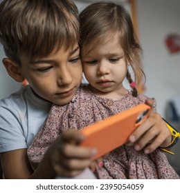 Siblings brother boy hold smartphone with girl sister children use mobile phone smartphone at home in room watch video make a call or play online games leisure family concept real people copy space - Shutterstock ID 2395054059