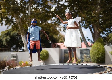 Siblings in costumes jumping on trampoline at lawn - Powered by Shutterstock