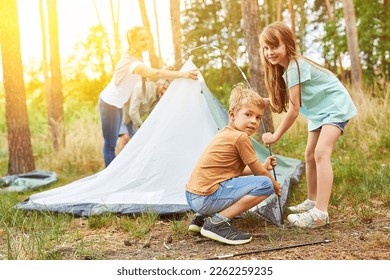 Siblings helping parents setting up tent while family camping in summer - Powered by Shutterstock