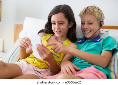 Siblings listening to music while using mobile phone on bed at home