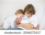 Siblings meet newborn baby in hospital. Child holding new infant brother for the first time. Kids visit mother in labor and delivery ward after birth of new baby. Sibling love. Family bonding.