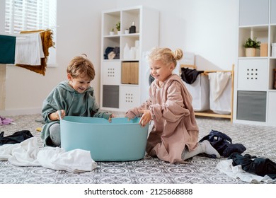 Siblings Play In Laundry Room, Bathroom With Dirty Clothes To Be Sorted, Kids Have Thrown All The Stuff Out Of The Bowl And Are Going To Hide In It From Mom