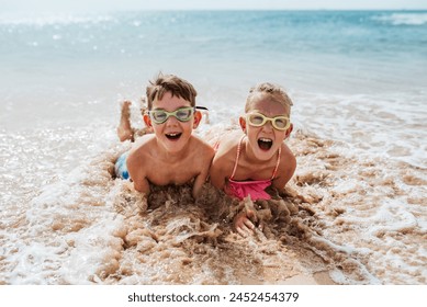 Siblings playing on beach, lying in water, having fun. Smilling girl and boy in swimsuits, swimming googles on sandy beach of Canary islands. Concept of family beach summer vacation with kids. - Powered by Shutterstock