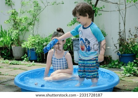 Siblings playing in a shallow pool in the backyard