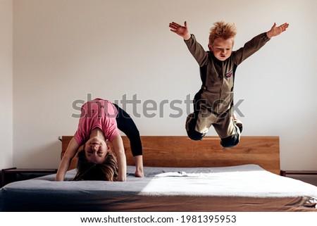siblings playing in their parent's bedroom. kid aviator flying on the bed. girl athlete doing the bridge, yoga position. Playful children. 