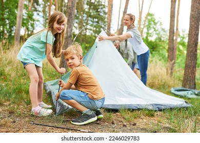 Siblings setting up tent for camping with parents in forest during summer vacation - Powered by Shutterstock