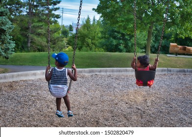 Siblings sitting on swings together at the park.