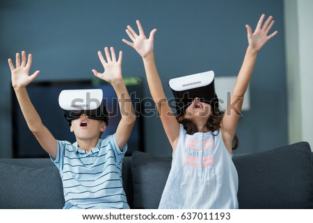Siblings using virtual reality headset in living room at home