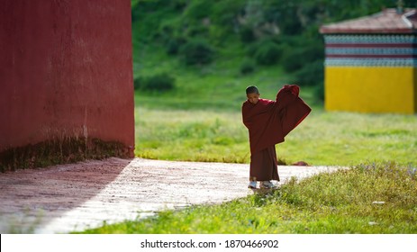Sichuan, China. July 27, 2015. Seda Wuming Buddhist College in Western Sichuan, China. A Tibetan Buddhist boy in red traditional costume walks alone in a sunny summer day.