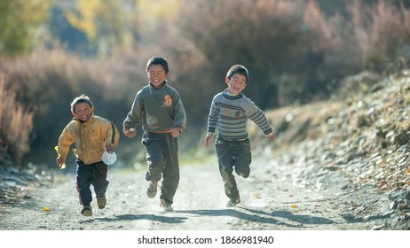 Sichuan, China. Nov 6, 2011. Rural Area Of Xinduqiao. Three Chinese Boys Running And Laughing Happily On The Mud Road Under The Sunshine. 