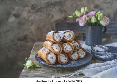 Sicilian cannoli deep fried pastry tubes on wooden rustic table with a sweet ricotta cream and dried candied fruits. Homemade Italian dessert on blue plate with flowers. Copy space, selective focus.