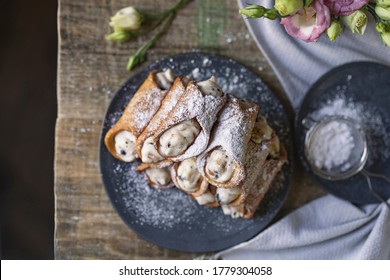 Sicilian cannoli deep fried pastry tubes on wooden rustic table with a sweet ricotta cream and dried candied fruits. Homemade Italian dessert on blue plate with flowers. Copy space, top view.