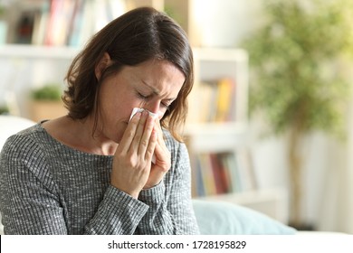 Sick adult woman blowing nose with tissue sitting on the couch at home