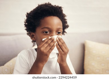 Sick african american boy with blowing nose into tissue. Child suffering from running nose or sneezing and covering his nose while sitting at home. Little boy suffering from cold or flu