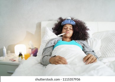 Sick African American Girl With Flu In Bedroom At Home. Ill Young Black Woman With Cold, Lying In Bed And Holding A Thermometer In Her Mouth.