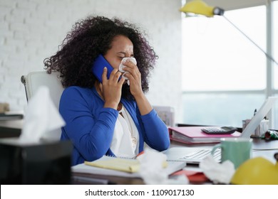 Sick African American Girl Working From Home Office. Ill Young Black Woman With Cold, Talking On Mobile Phone And Sneezing For Flu Virus.