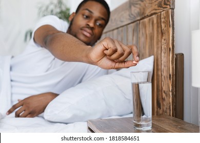 Sick African American Man Taking Medicine, Putting Pill Into Glass Of Water Lying In Bed At Home. Flu, Cold And Influenza Disease Medication Treatment Concept. Selective Focus