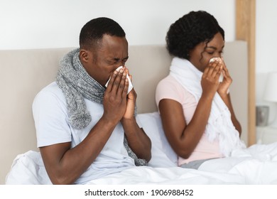 Sick African American Man And Woman Got Coronavirus Or Cold, Sneezing Their Noses, Staying In Bed During Illness. Black Couple With Scarfs Around Their Necks Having Flu. Cold And Flu Concept