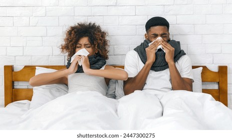 Sick african-american couple blowing noses in bed, having flu together, copy space - Powered by Shutterstock