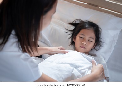Sick asian child girl get sick and sleep on the bed, mother taking care and cover the blanket on her daughter at home. - Shutterstock ID 1828603070