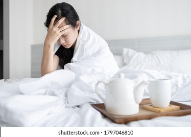 Sick asian child girl is holding temple with her hand while sitting in bed feeling tired,uncomfortable,drowsy,dizzy after waking up in the morning,woman have a headache,aching pain touching her head