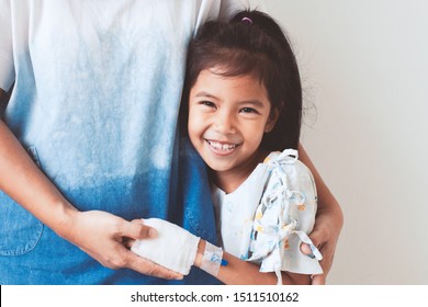 Sick Asian Child Girl Who Have IV Solution Bandaged Smiling And  Hugging Her Mother With Love In The Hospital