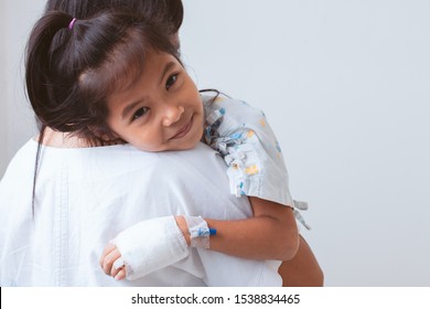 Sick Asian Child Girl Who Have IV Solution Bandaged Smiling And  Hugging Her Mother With Love In The Hospital