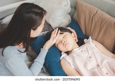 Sick Asian Girl Daughter Sleeping On The Couch With Fever While Mother Checking Temperature On Her Forehead