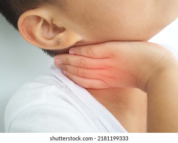 Sick Asian Kid Touching His Painful Neck, Sore Throat And Flu, Throat Infection On White Background. Closeup Photo, Blurred.