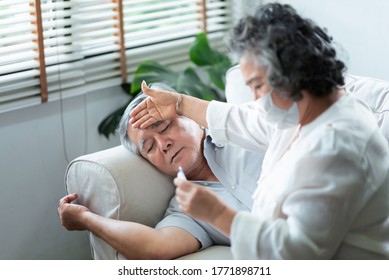 Sick Asian Senior man have flu lying on couch while his Wife in face mask holding and checking temperature at thermometer. Coronavirus or Covid-19 Pandemic, illness, disease, Cold in Elderly people - Powered by Shutterstock