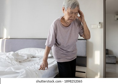 Sick asian senior woman suffering from dizziness,sensation of spinning around,losing her balance,old elderly touching her temple with eyes closed after getting up from bed,vertigo while standing up