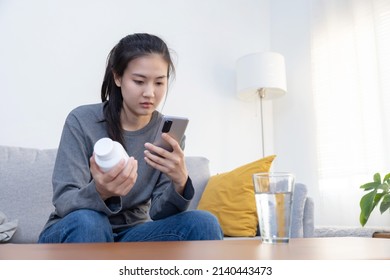 Sick Asian Woman Read Medicine Prescription On Her Mobilephone While Holding Pills Bottle On The Sofa