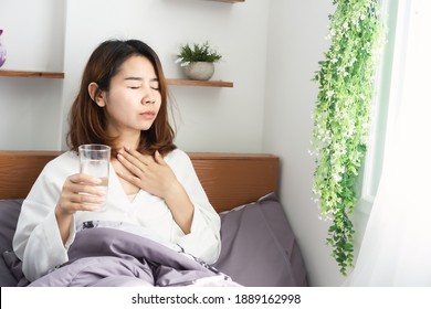 sick Asian woman suffering from sore throat drinking water in her bed 