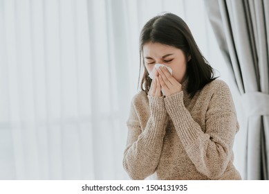 Sick Asian Woman Using A Tissue To Sneeze And Blowing Her Nose In Winter At Home. Her Getting Sick With Flu And Cold.

