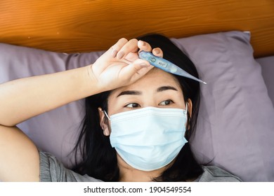 Sick Asian Woman Wearing Face Mask Hand Holding Thermometer Having  Fever, High Body Temperature Laying Down In Bed