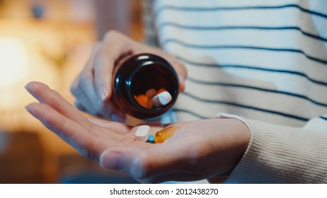 Sick Asian Young Lady Holding Pill Take A Look Medicine Sit On Couch At Home Night. Girl Taking Medicine After Doctor Order, Quarantine At Home, Coronavirus Social Distancing Healthcare Concept.