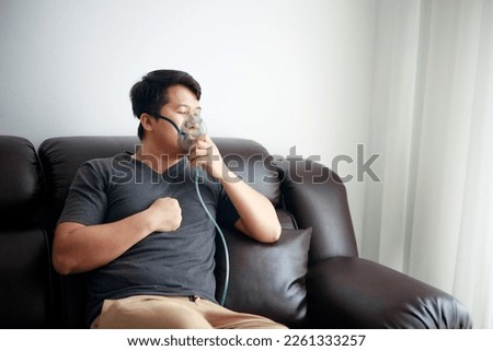 Sick Asian young man using nebulizer for asthma and respiratory diseases at home.
