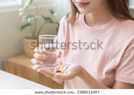 Sick, asian young woman, girl hand holding pill capsule, painkiller medicine from stomach pain, head ache, pain for treatment, take drug or vitamin and glass of water at home, pharmacy and health care