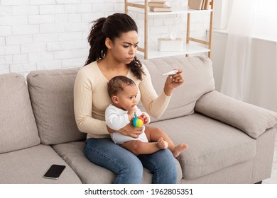 Sick Baby Having Fever. Concerned Black Mom Measuring Little Toddler's Temperature With Thermometer Caring For Ill Son Sitting On Sofa At Home. Child Care And Infant's Health Problem Concept