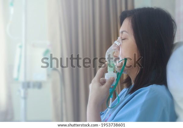 Sick beautiful female in blue cloth hold
nasal mask with respiratory problem in hospital room. Asian woman
patient inhalation therapy by the mask of inhaler with soft stream
smoke from bronchodilator.