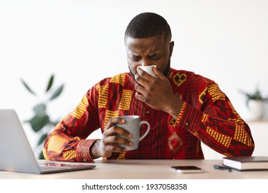 Sick Black Man Sneezing At Workplace In Office, Blowing Nose To Napkin