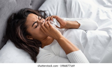 Sick Black Woman Suffering From Running Stuffy Nose And Sore Throat. Upset Ill African American Lady Lying In Bed, Blowing Her Nose Using Paper Napkin Tissue, Banner. Cold And Flu Concept