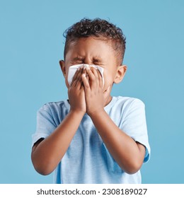 Sick, blowing nose and a boy with a tissue with covid isolated on a blue background in a studio. Health, young and a little boy with an allergy problem, virus and sneezing from a cold on a backdrop - Powered by Shutterstock