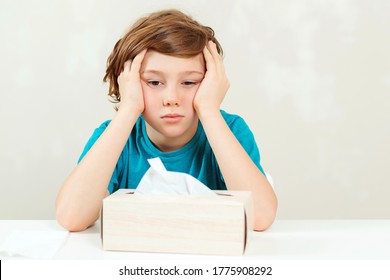 Sick Boy Sitting At The Desk. Kid Using Paper Napkins. Allergic Kid, Flu Season. Box With Nose Napkins. Boy Has A Virus, Runny Nose And Headache. Schoolboy Blowing Runny Nose.