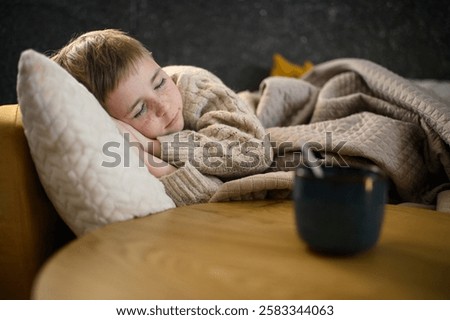 A sick boy sleeps in bed under a blanket, resting. On the table beside him, a cup of tea with honey and lemon remains, offering warmth and comfort.