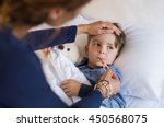 Sick boy with thermometer laying in bed and mother hand taking temperature. Mother checking temperature of her sick son who has thermometer in his mouth. Sick child with fever and illness in bed.